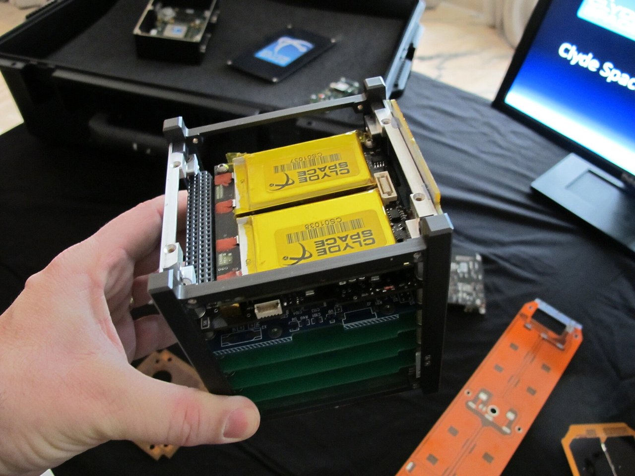 Eine Hand hält eine 1U-CubeSat-Struktur mit Akkus und Leiterplatten; Svobodat, CC BY-SA 3.0
